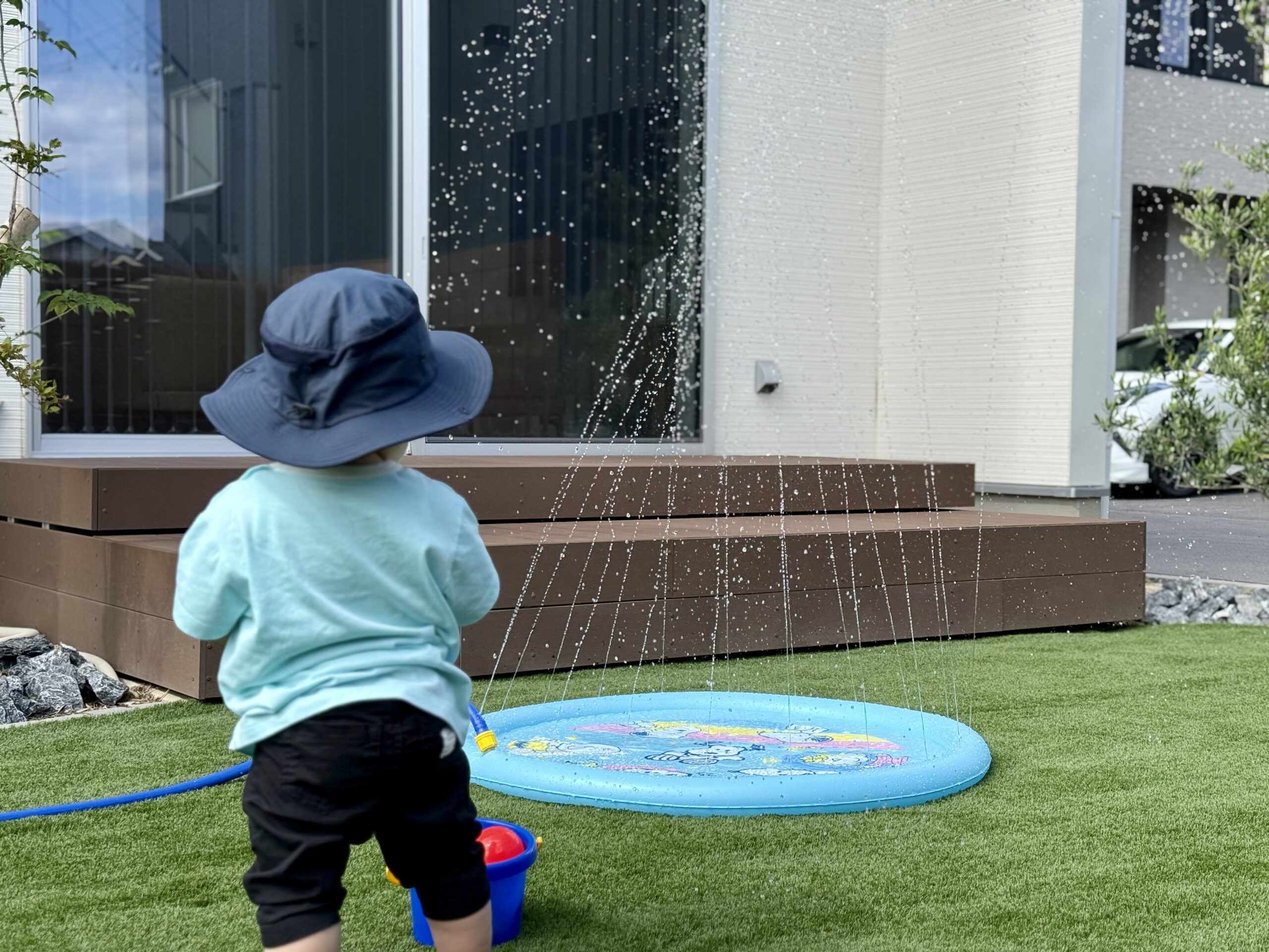 噴水マットで遊ぶ1歳の子どもの後ろ姿