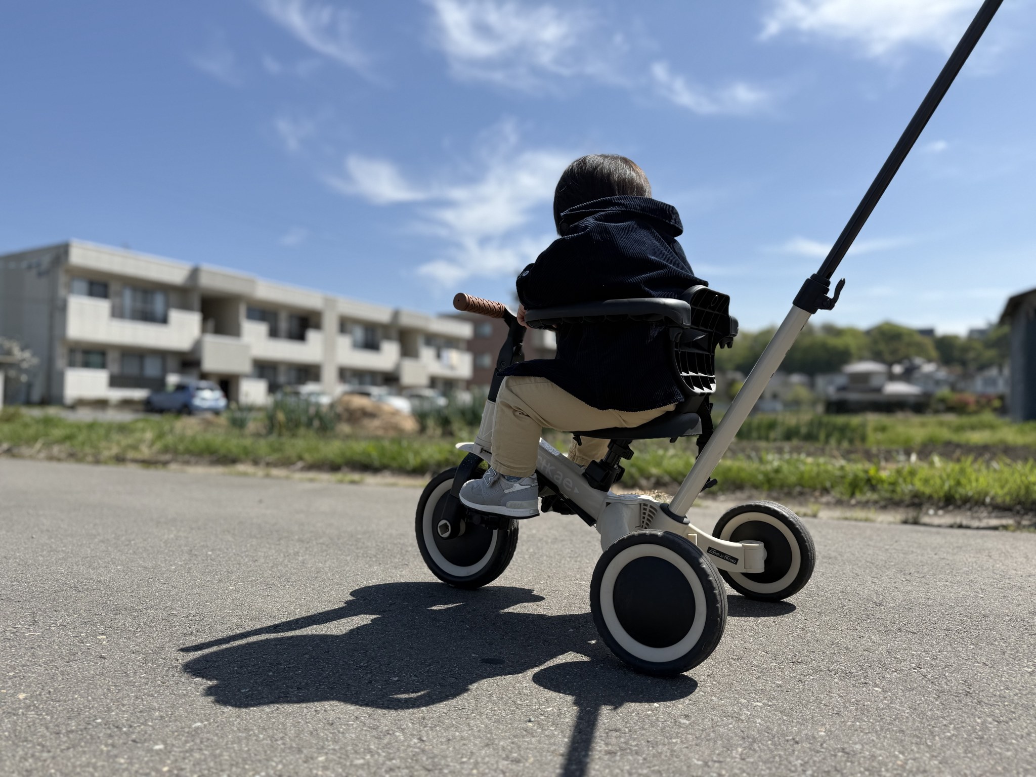 青空の下、押し棒付き三輪車に乗る1歳の息子の後ろ姿