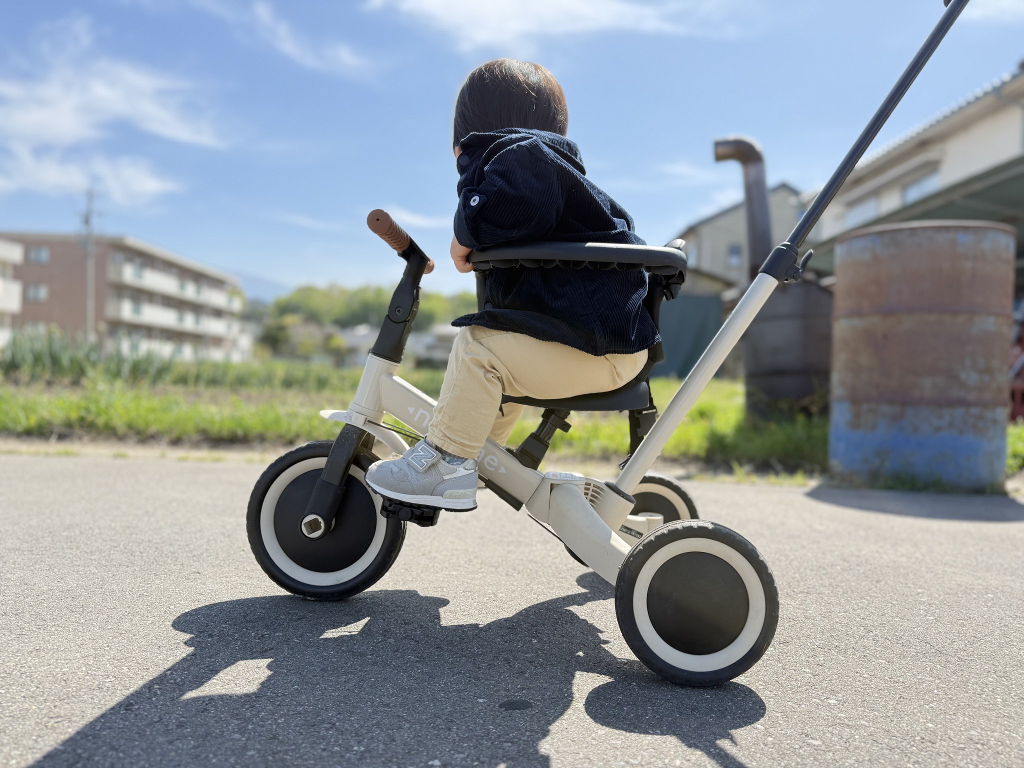 三輪車のシートに座る1歳児。足はまだペダルに届くだけ