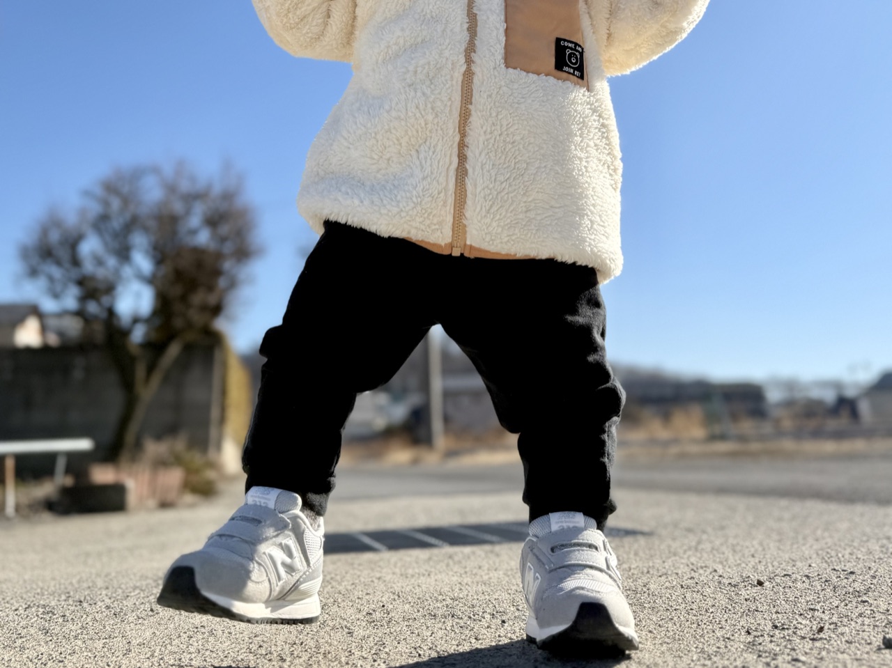 白いニューバランスのファーストシューズを履いて青空の下を歩く子どもの足元