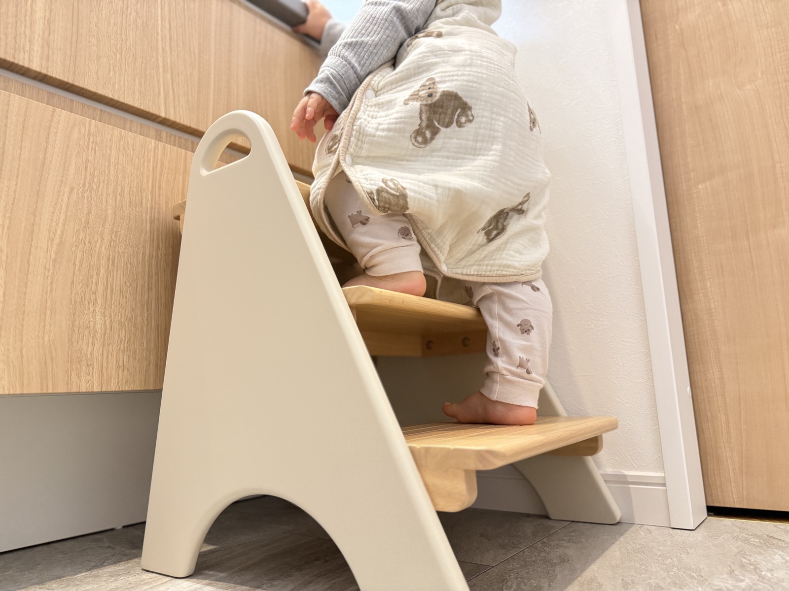 踏み台の段に自分の足で立つ1歳の子どもの足元
