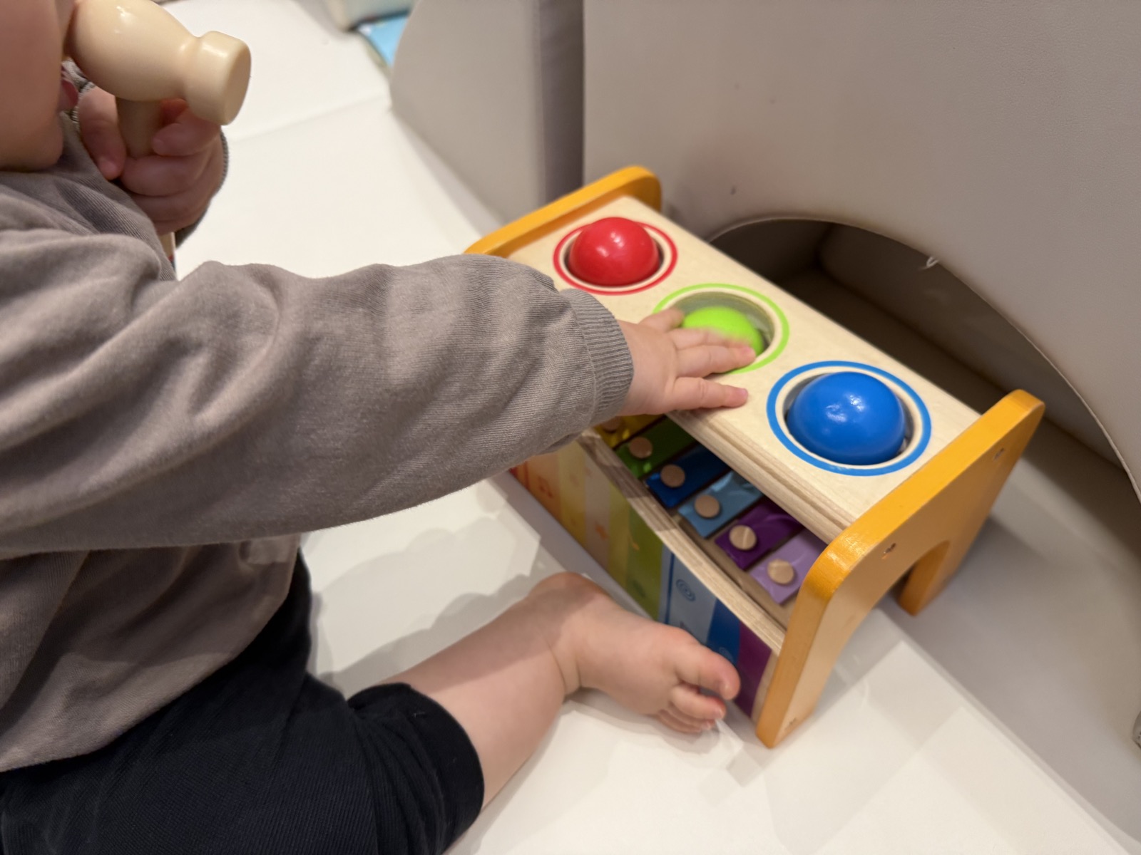 1歳の子どもが木のハンマーを持ち、パウンドアンドタップベンチのボールに手を伸ばしているところ